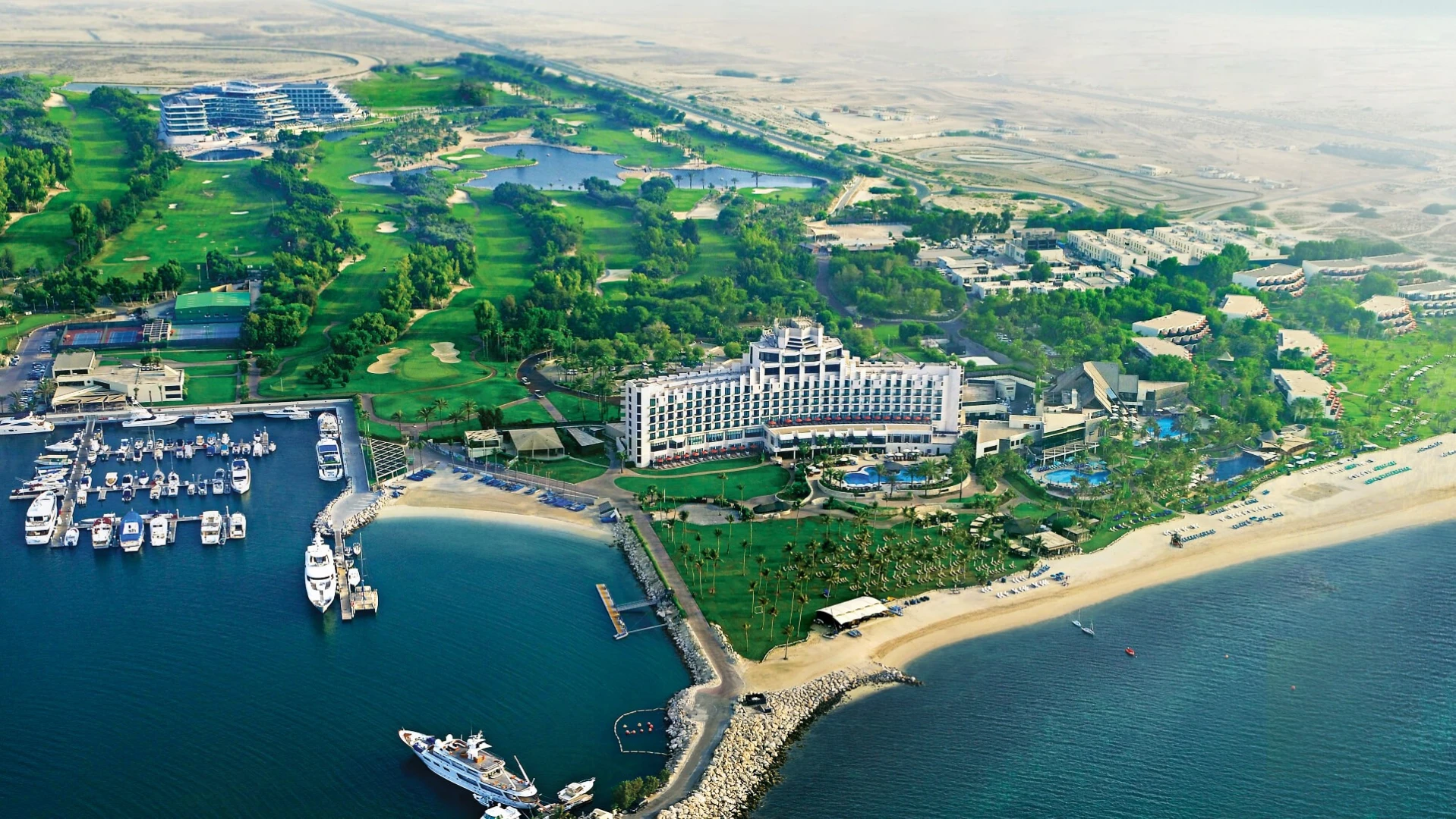 Aerial view of JA Beach Hotel, Dubai with marina and greenery.