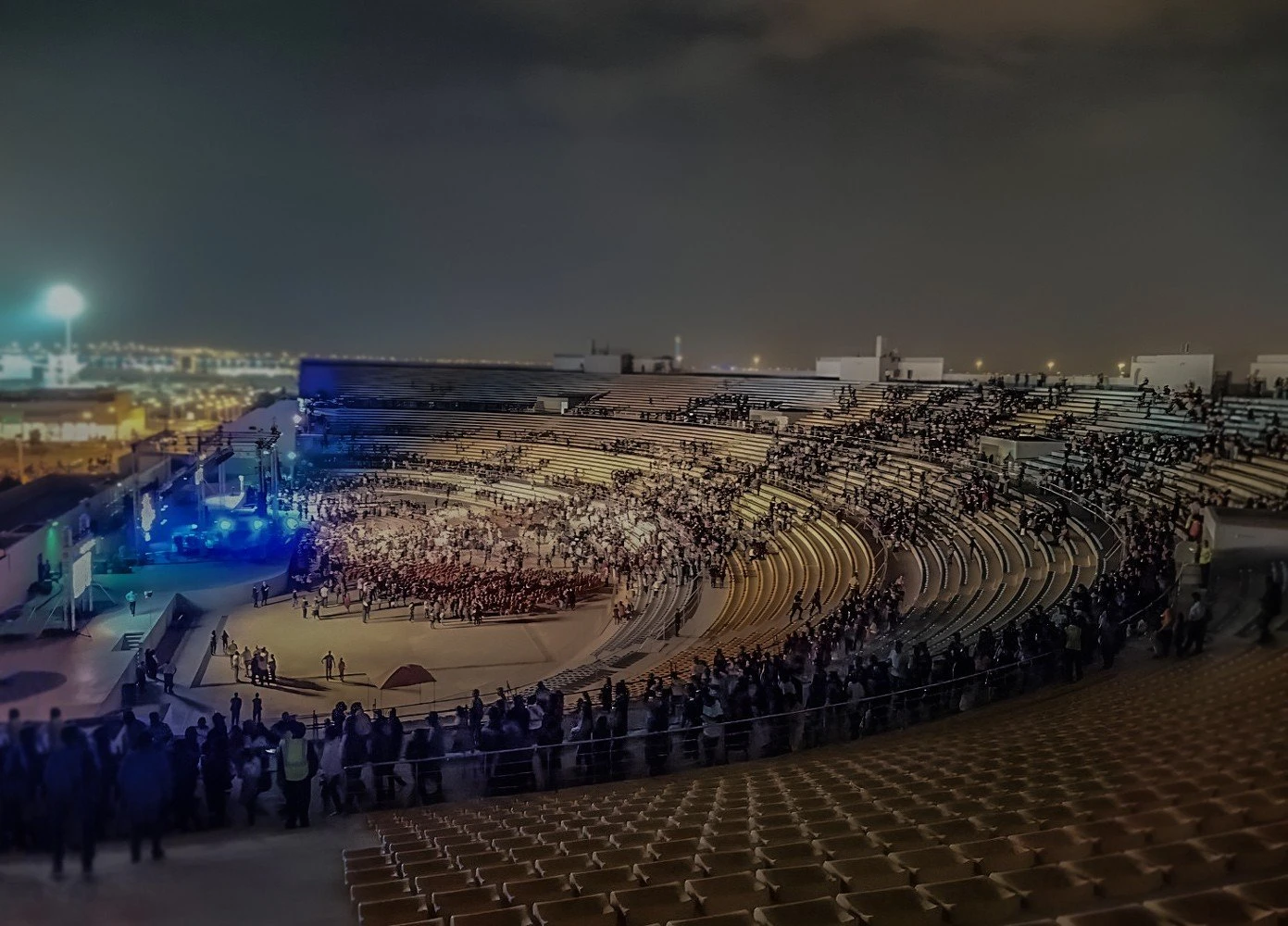 Crowded Asian Town Amphitheater at night, Doha skyline visible.